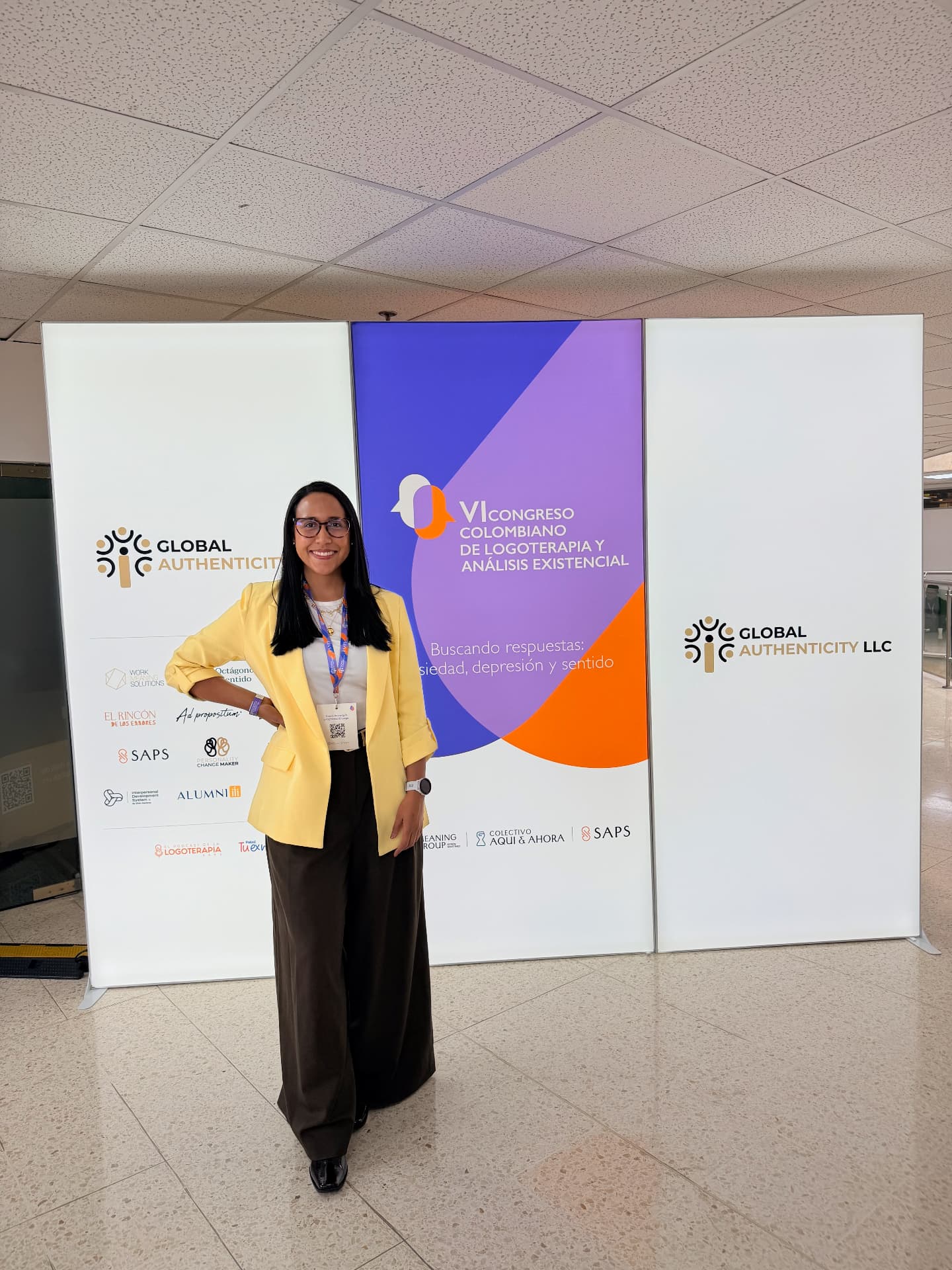 Lina de blazer amarillo, de pie frente a la publicidad del VI Congreso Colombiano de Logoterapia
